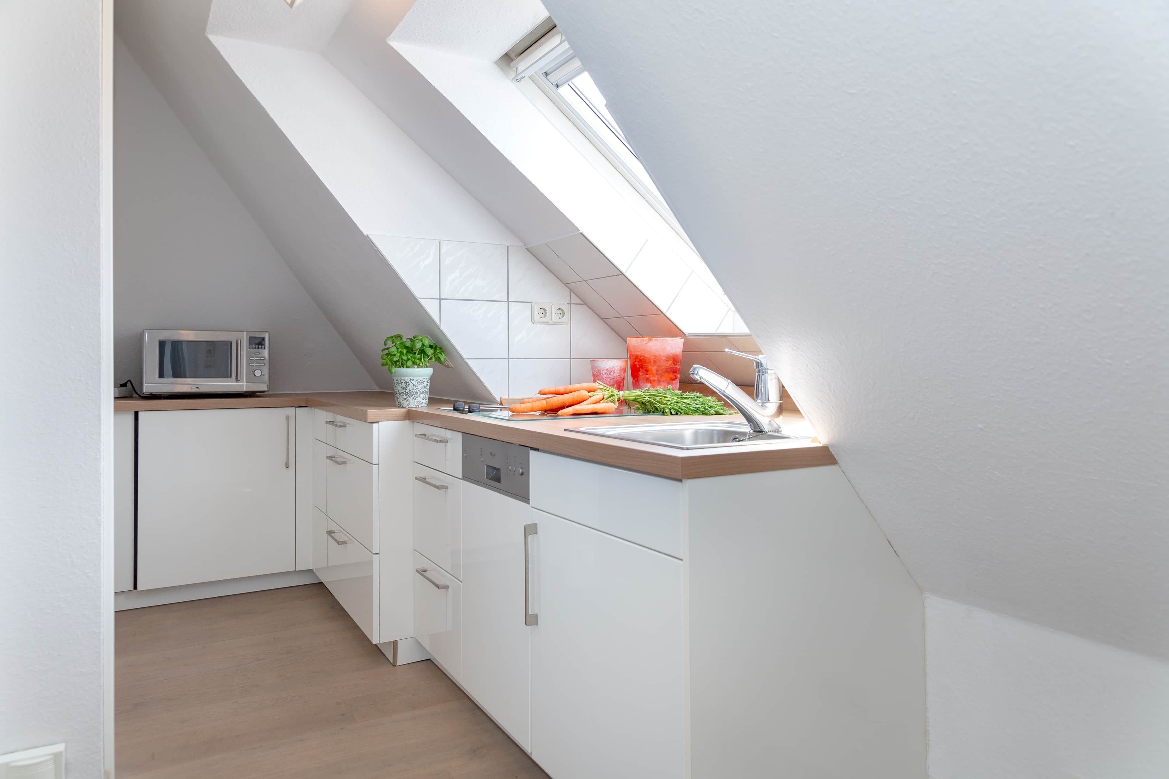 Una cocina moderna con armarios blancos, un microondas, un lavamanos y una ventana sobre la encimera.