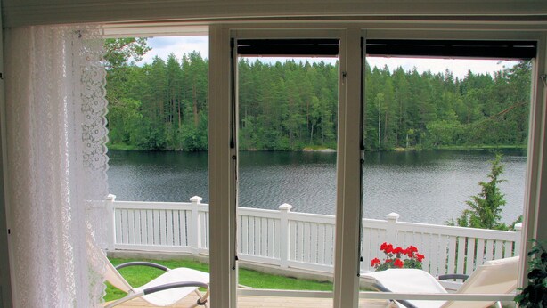 A deck with white railings and a view of a lake surrounded by trees.