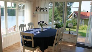 A dining area with a round table, white chairs, a blue tablecloth, and a vase with flowers.