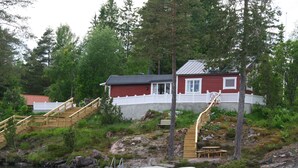 A cabin with a wooden staircase leading to a dock by a lake, surrounded by trees.