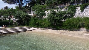 A clear beach with steps leading into the water, surrounded by greenery and a stone wall. - A romantic Mediterranean apartment (Barbat na Rabu)