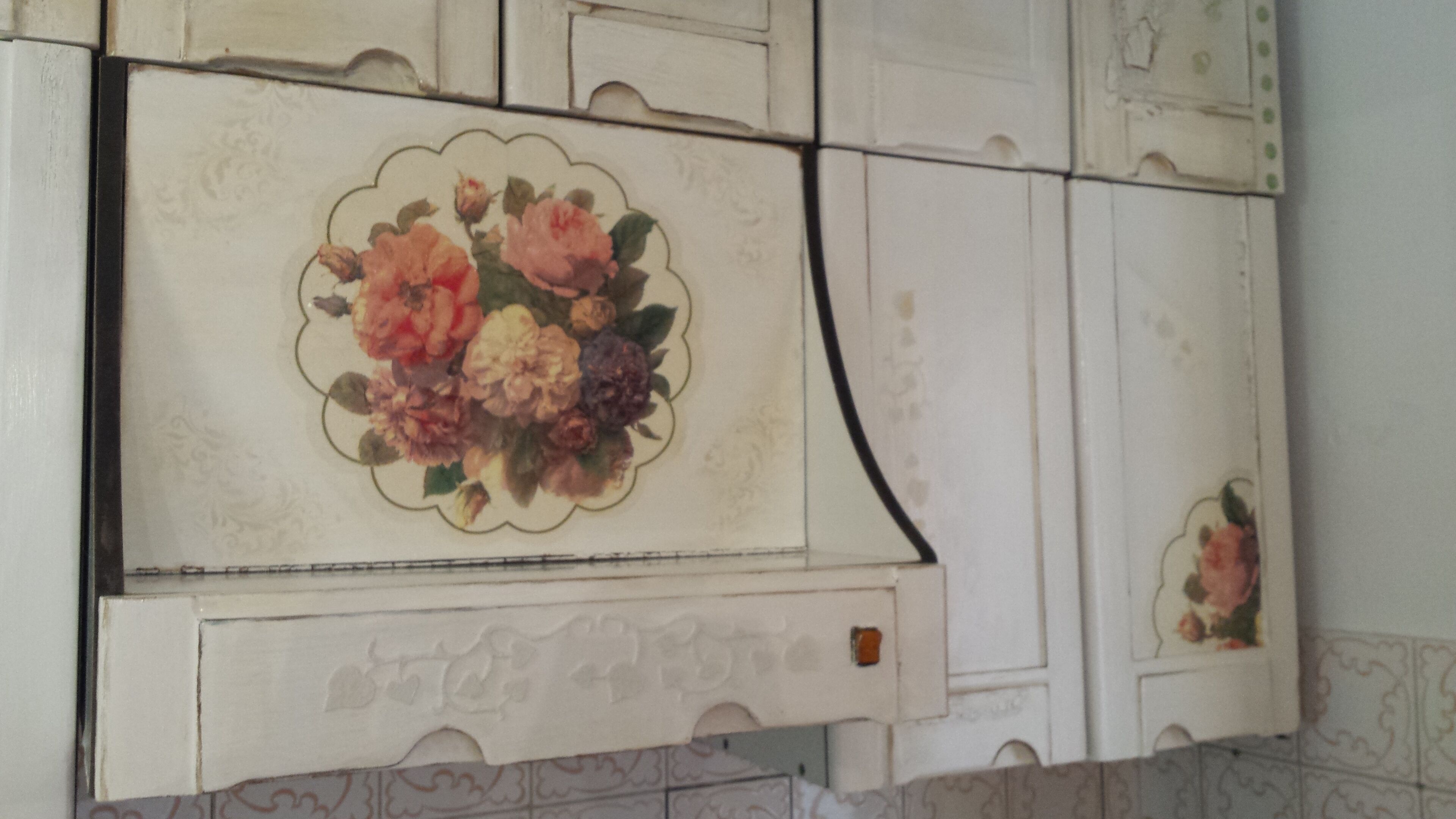A kitchen with white cabinets and a floral design on the upper cabinets.