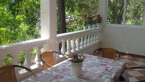 A balcony with a table covered in a patterned tablecloth, surrounded by wicker chairs, and potted plants with flowers. - A romantic Mediterranean apartment (Barbat na Rabu)