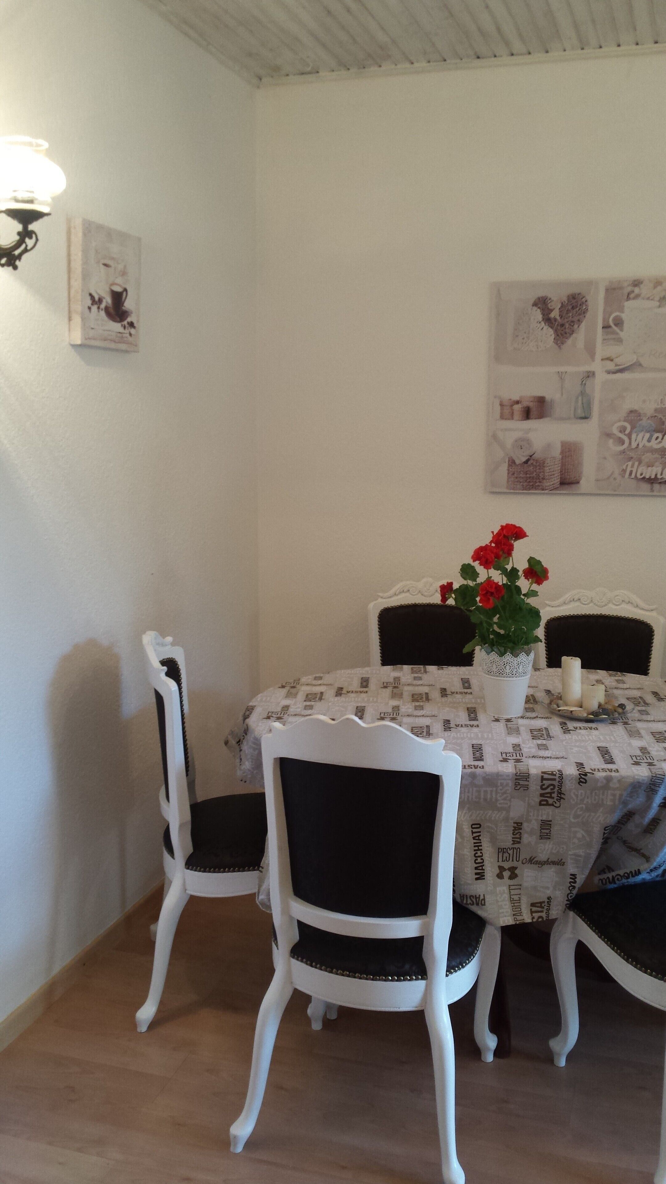 Un coin repas avec une table ronde, des chaises blanches, un vase avec des fleurs rouges et des éléments décoratifs sur les murs.