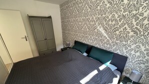 Un dormitorio con una cama grande, un armario, una mesita de noche y un papel tapiz estampado.