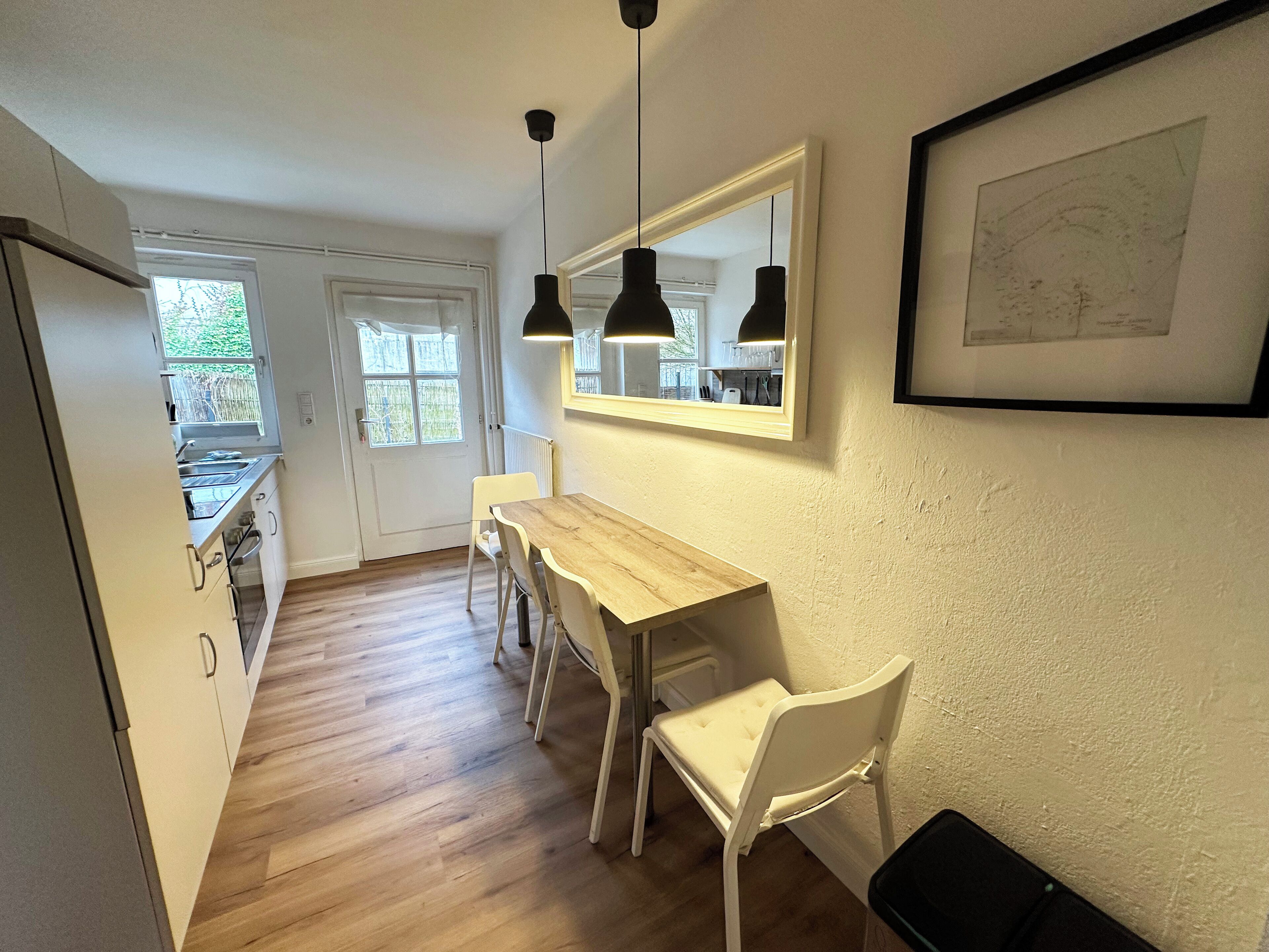 Eine moderne Küche mit einem Holztisch, weißen Stühlen, Pendelleuchten und einer an der Wand hängenden Karte.