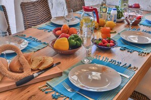Une table de salle à manger en bois, mise avec des assiettes, des corbeilles de fruits, une carafe et du pain.