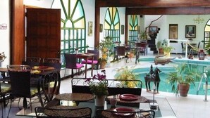 Un'ampia area interna con piscina, tavoli da pranzo, sedie e piante in vaso.