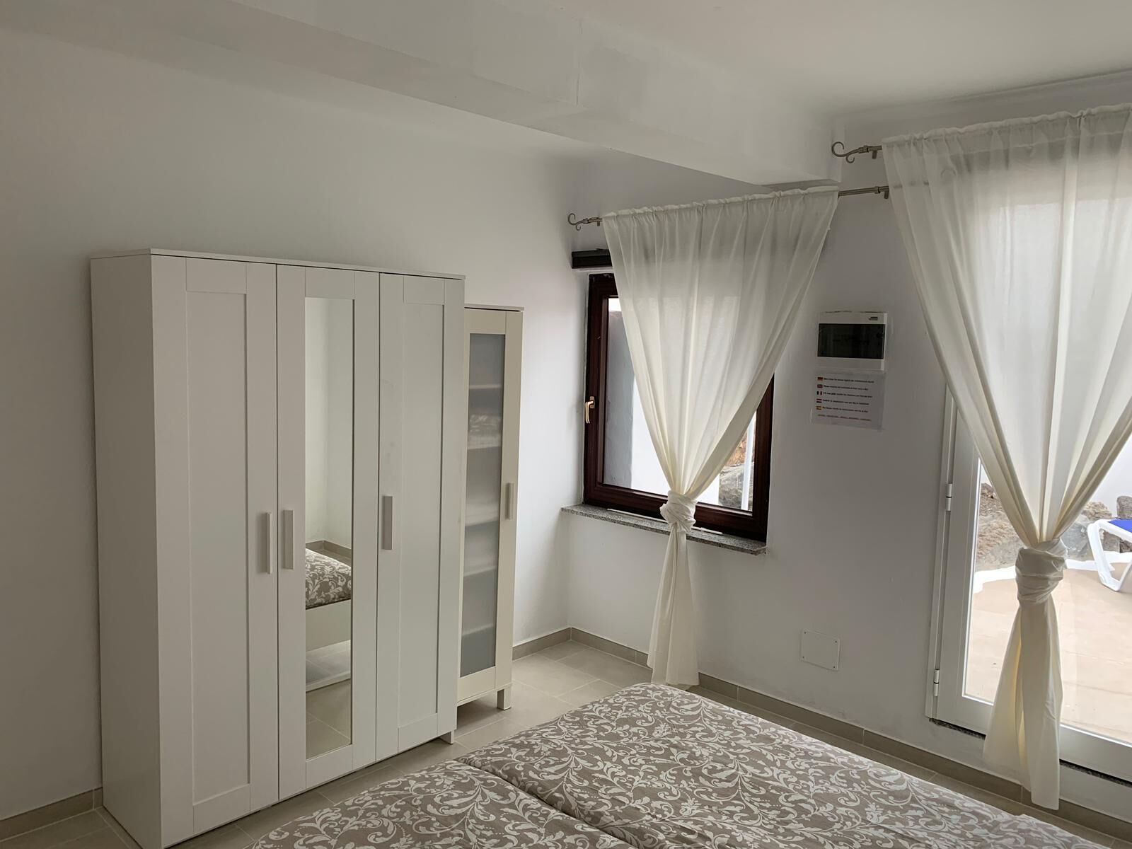 Quarto com guarda-roupa, cama e janela com cortinas.