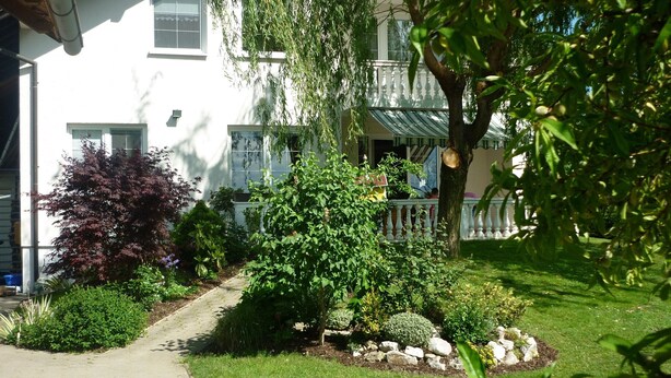 Un immeuble résidentiel doté d’un jardin bien entretenu, d’un chemin menant à l’entrée et d’un porche avec une balustrade.