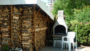 Un espace extérieur doté d’une cheminée en pierre, d’une chaise en plastique blanche et d’une pile de bois de chauffage.