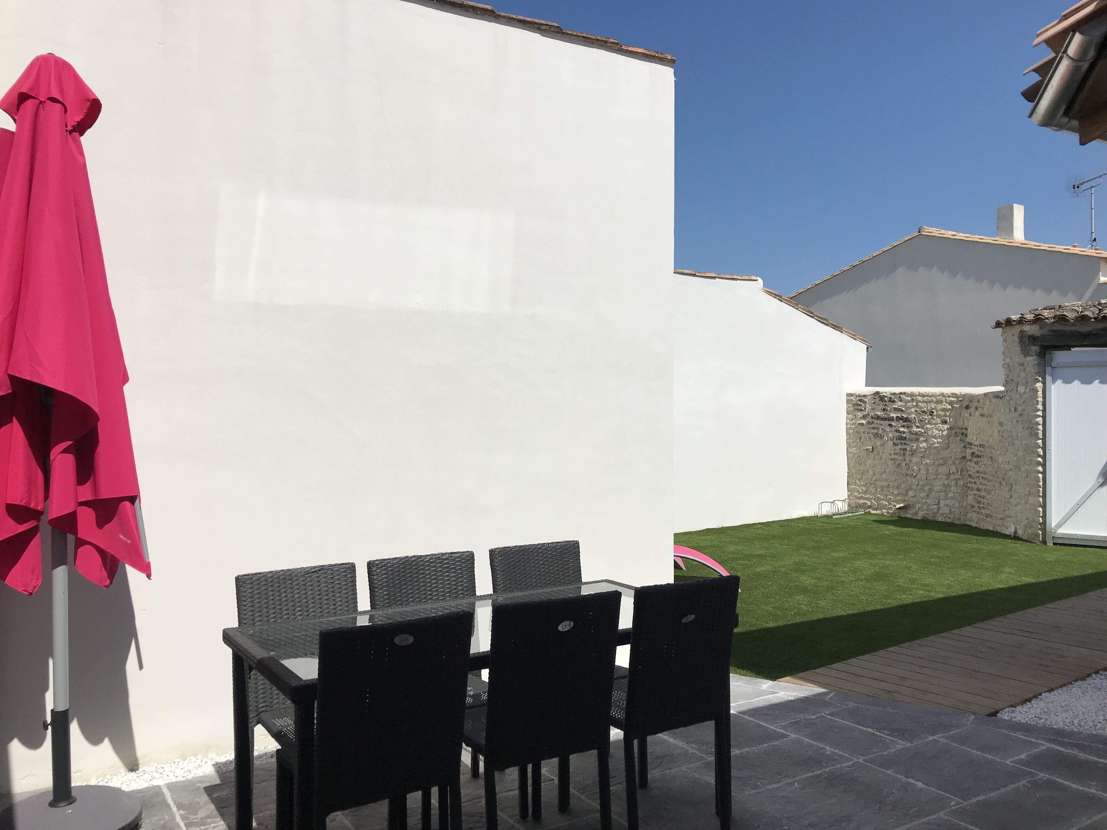 Une terrasse extérieure avec une table et des chaises, un parasol rouge et un mur blanc.