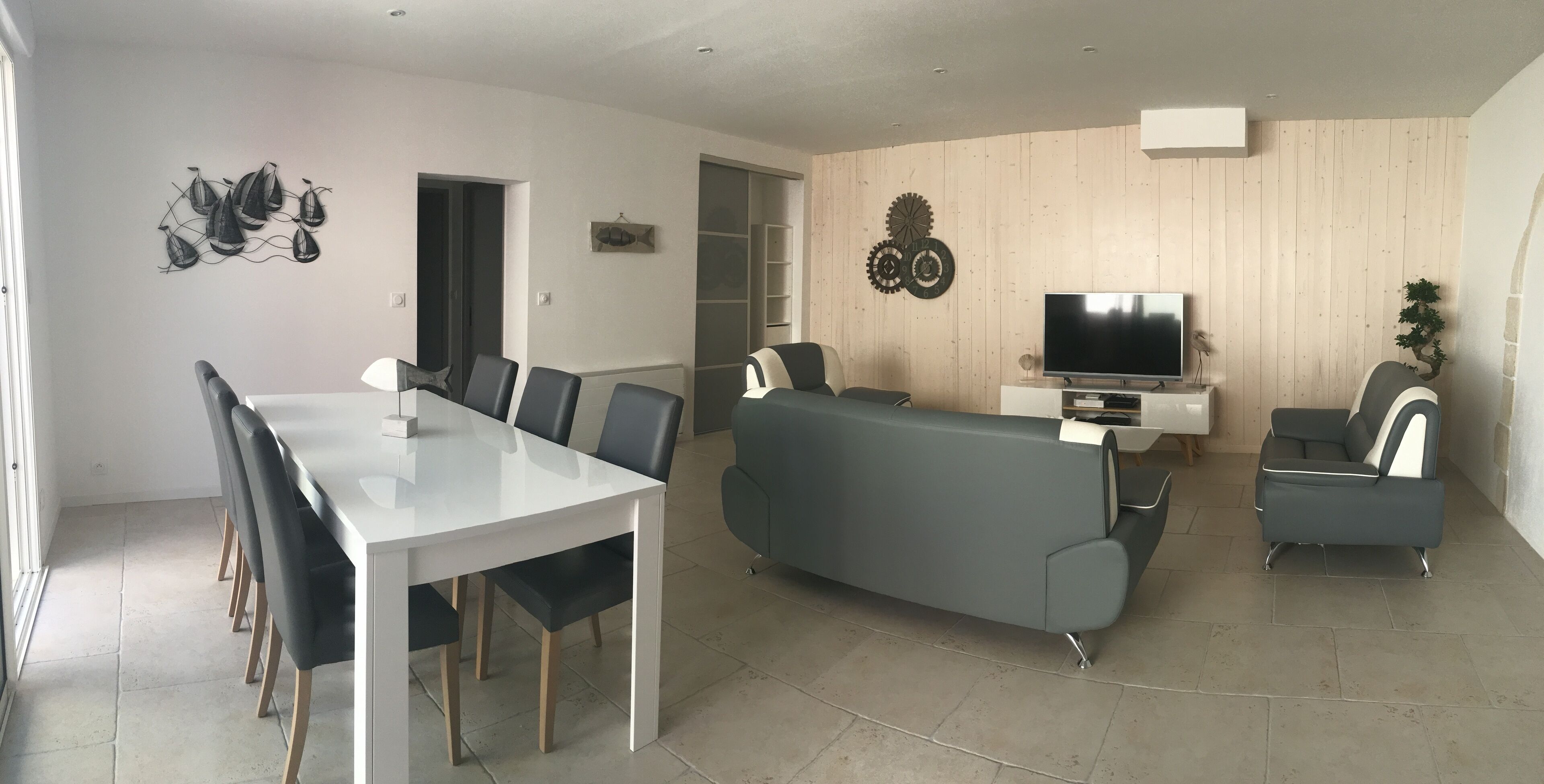 Un salon moderne avec une table à manger blanche, un canapé gris et deux fauteuils.