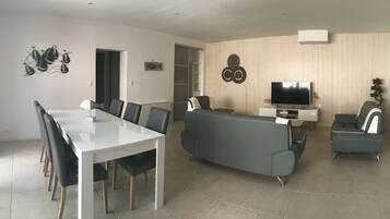 Un salon moderne avec une table à manger blanche, un canapé gris et deux fauteuils.