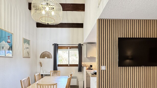 Un coin repas avec une table et des chaises en bois, un luminaire suspendu et une fenêtre avec des rideaux.