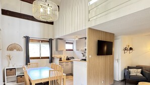 Un salon moderne comprenant un coin repas, une cuisine et un téléviseur fixé au mur.