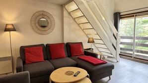 Un salon moderne avec un canapé gris, des coussins rouges, une table basse ronde en bois et un escalier menant à un niveau supérieur.