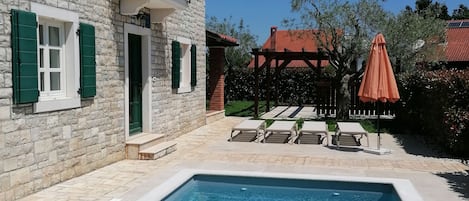A swimming pool with a stone wall and a balcony with green shutters.