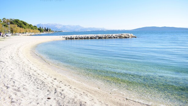 A clear beach with a rocky breakwater, calm water, and a distant mountain range. - SPECIAL OFFER! Studio APARTMENT with BALCONY (Kaštel Stari)