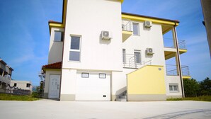 A two-story building with a white facade and yellow accents, featuring a garage door, multiple windows, and an air conditioning unit. - SPECIAL OFFER! Studio APARTMENT with BALCONY (Kaštel Stari)