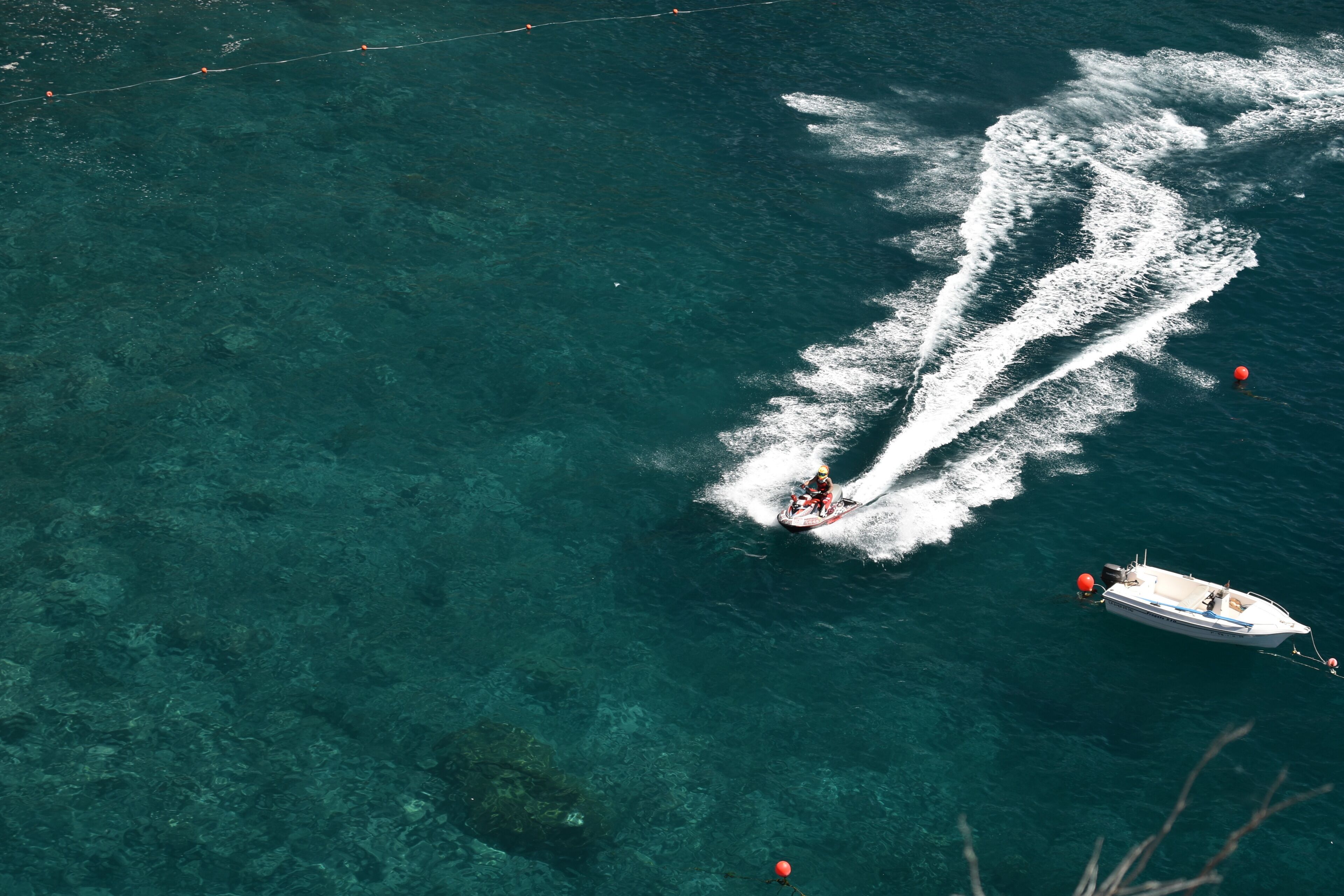 Un bote dejando estela, una persona en un jet ski y una boya.