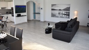 Ein modernes Wohnzimmer mit einer schwarzen Couch, einem Glastisch und einem an der Wand befestigten Flachbildfernseher.