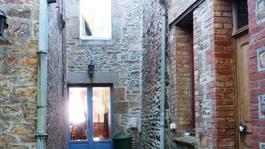 A narrow stone alleyway with a blue door, a wooden door, and a trash bin. - Charming village house, Mt St Michel Bay (Genêts)