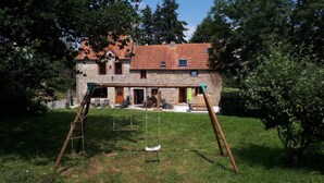 A stone building with a red-tiled roof, a swing set, and a well-maintained lawn. - Gîte "le Marité", 4 people (Sartilly)