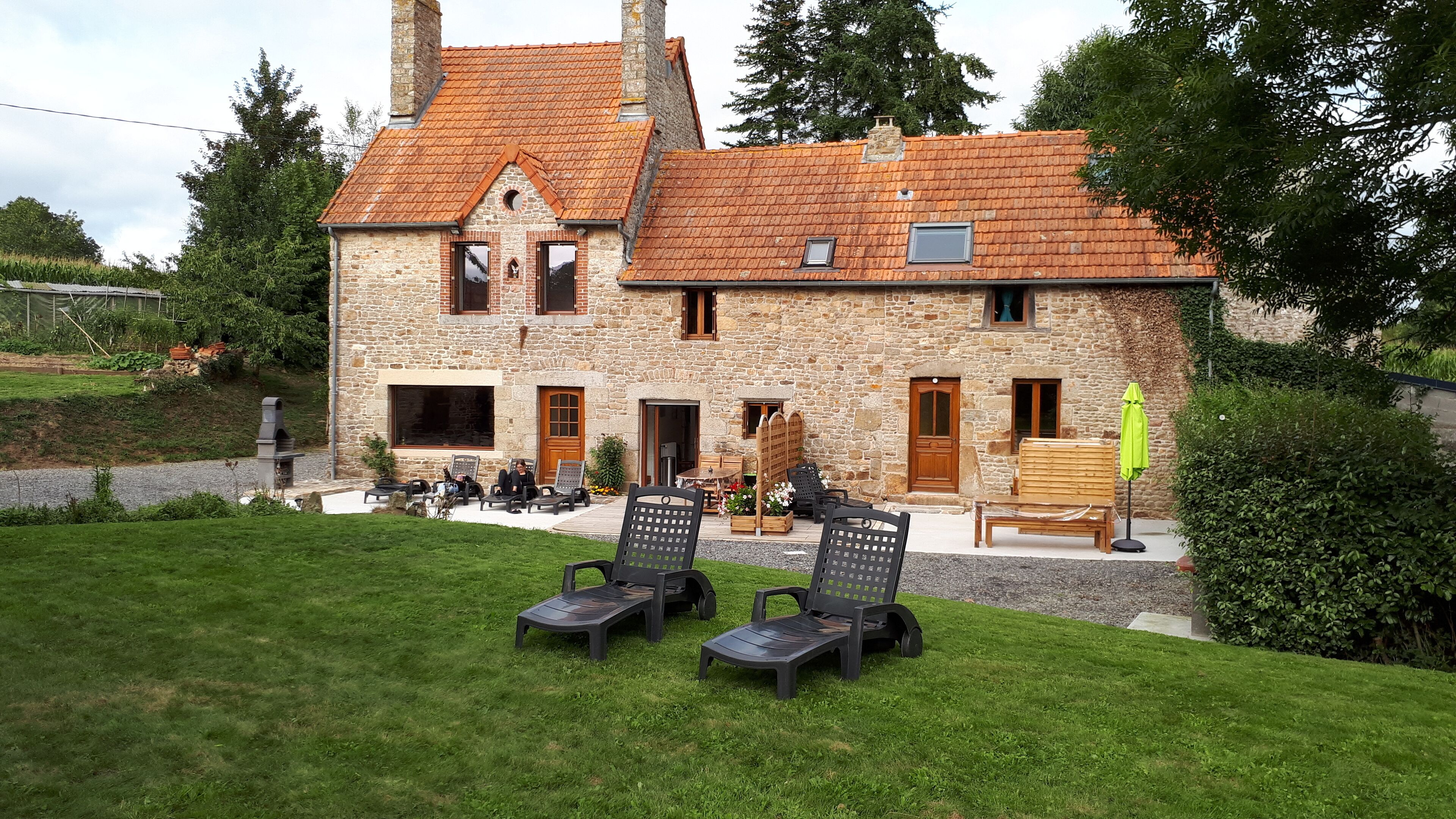 A stone building with a tiled roof, outdoor seating, and a grassy area.