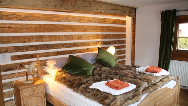 Ein hölzernes Bett mit einem Fellüberwurf, Kissen und einem Nachttisch mit Lampe.
