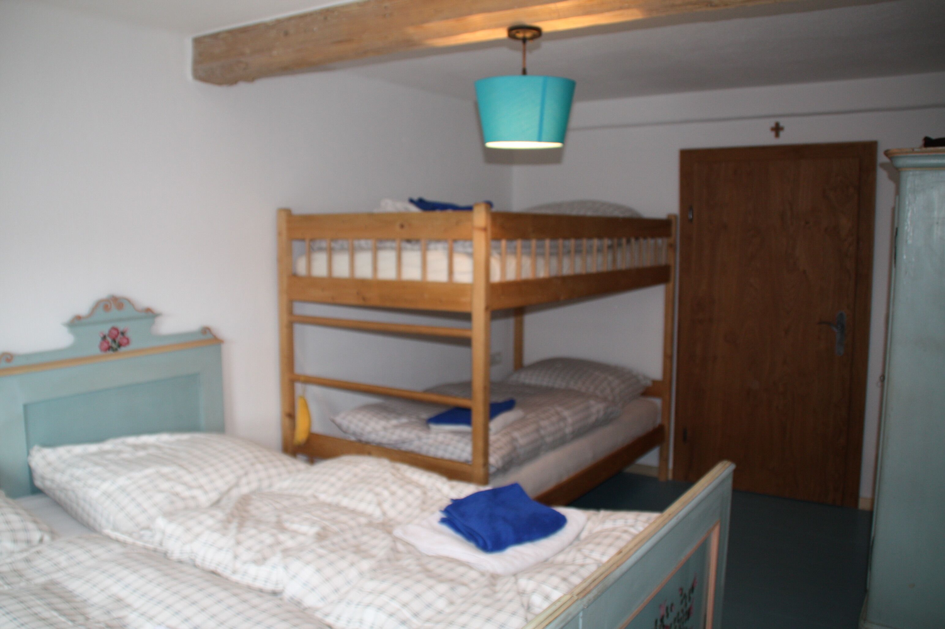 A bunk bed room with a wooden headboard, a small bedside table with a clock, and a door to the right.