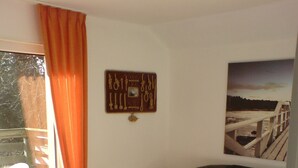 Un salon avec une table basse en bois, un canapé en cuir noir, une fenêtre avec des rideaux orange, un radiateur et un tableau accroché au mur.