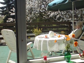 A patio with a table set for two, a chair, and a view of a garden with blooming flowers. - 'Zur Kajüte' cozy, private, central location. (Butjadingen)