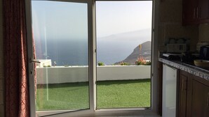 Ein Zimmer mit einer Schiebeglastür, die auf einen Balkon mit Blick aufs Meer und die Hügel führt.
