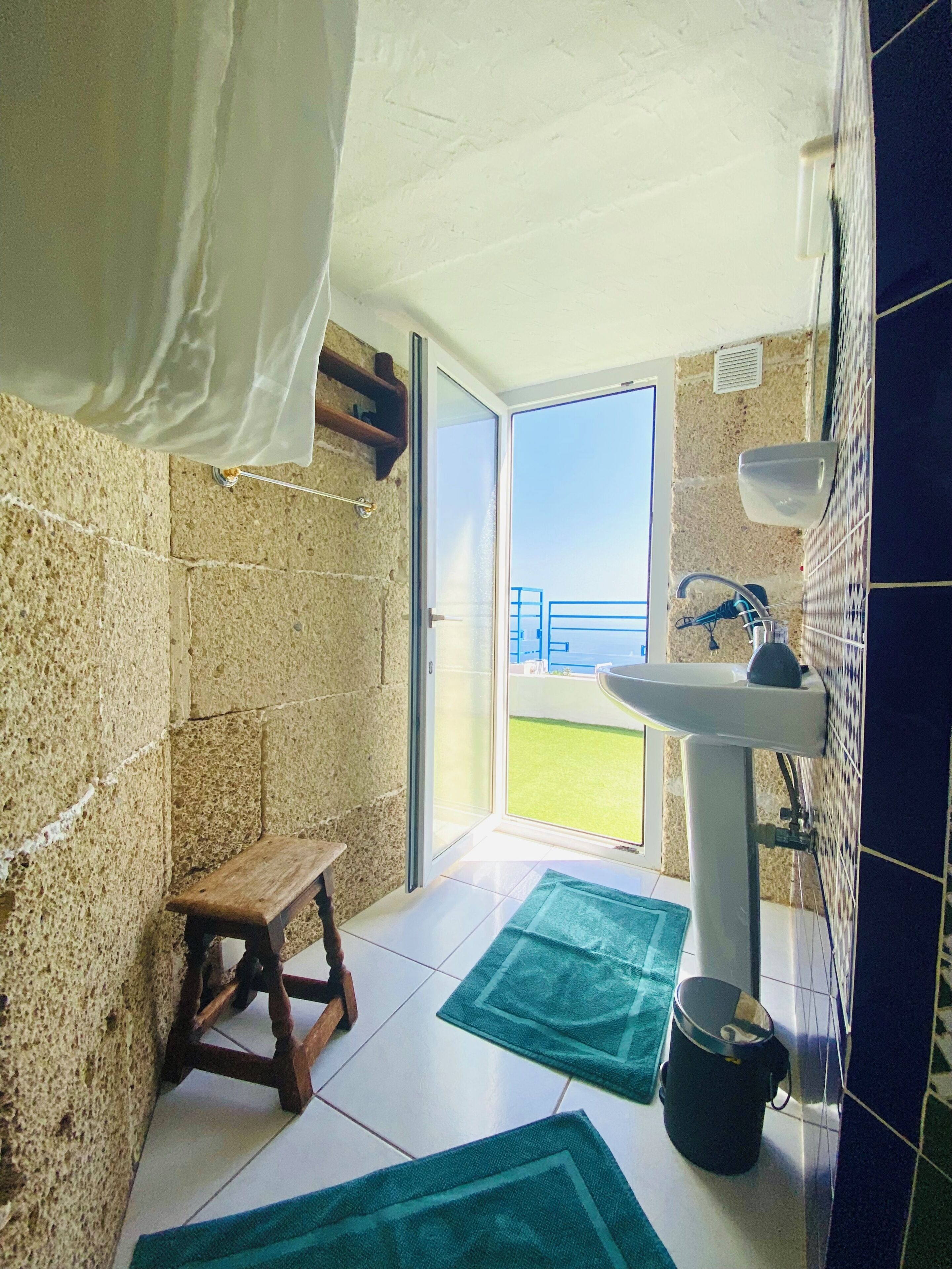 A bathroom with a stone wall, a wooden stool, a sink, and a view of the outdoors.