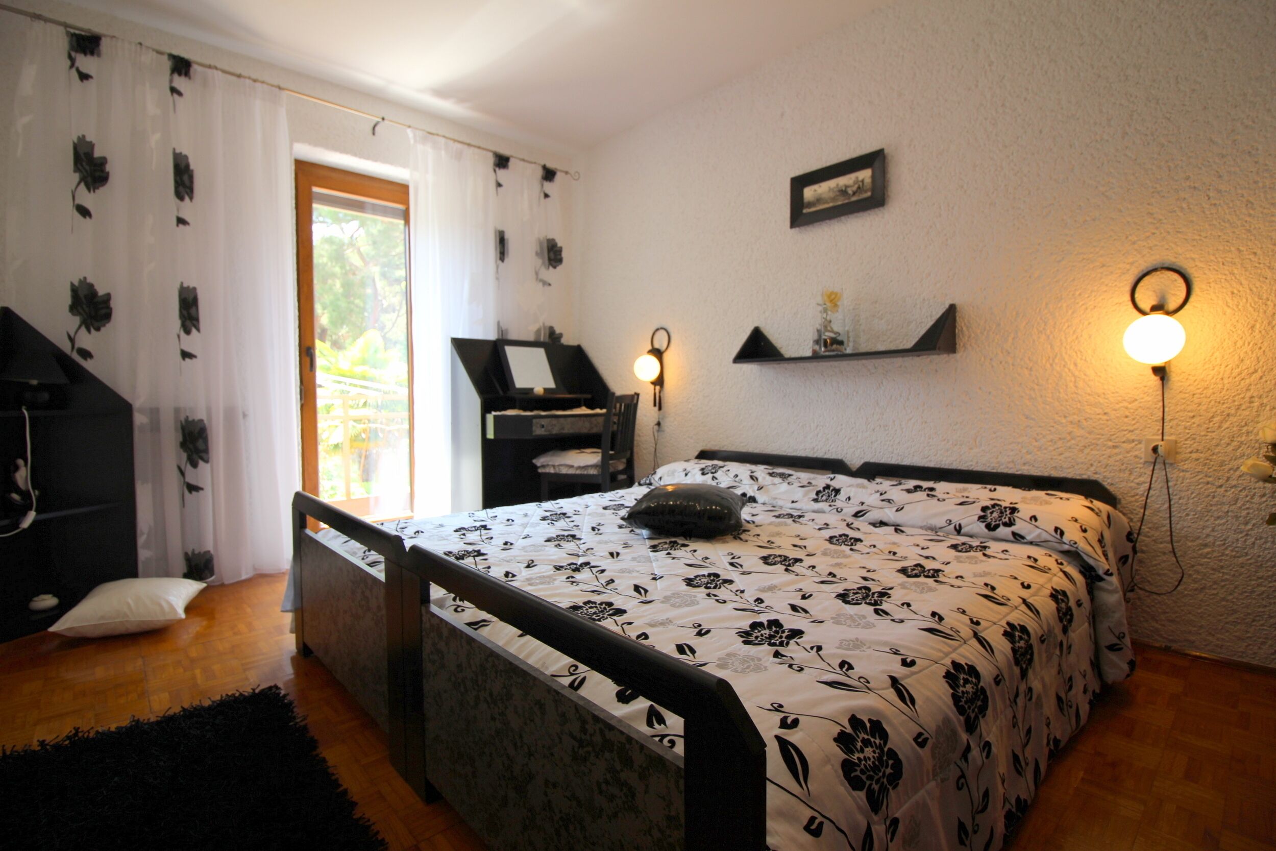 Une chambre à coucher avec un lit, un piano, un canapé noir, une petite étagère et une fenêtre avec des rideaux.