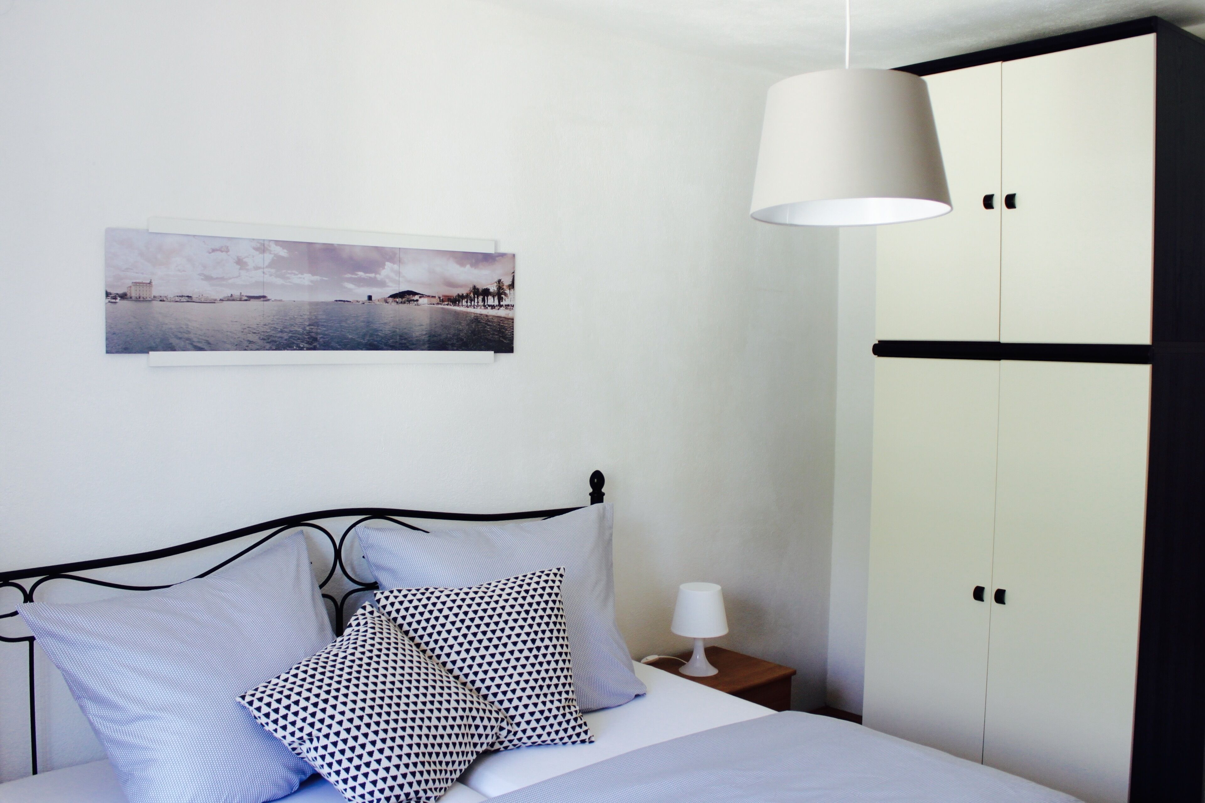 Une chambre à coucher comprenant un lit, une table de chevet, une lampe, une armoire et un tableau accroché au mur.