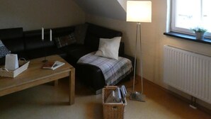 A cozy room with a wooden ceiling, a black sofa, a small table, a floor lamp, and a window with a view. - Romantic four-star holiday home in the style of a country-house (Pommern)