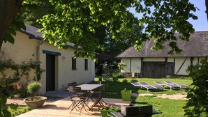 Un patio con mesa y sillas de madera, una parrilla y un pequeño jardín con plantas en macetas.