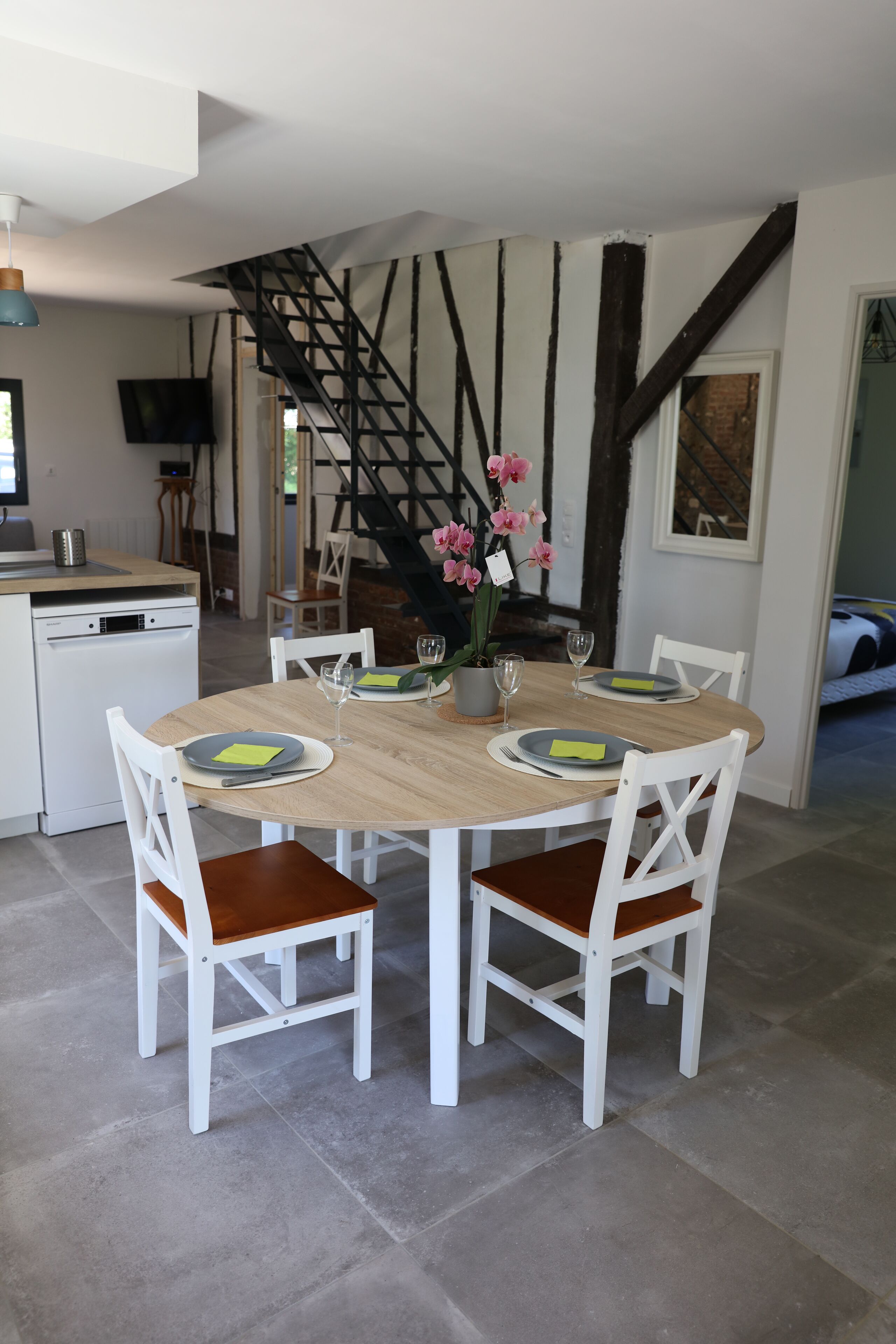Un coin repas avec une table ronde, des chaises blanches et un escalier en arrière-plan.
