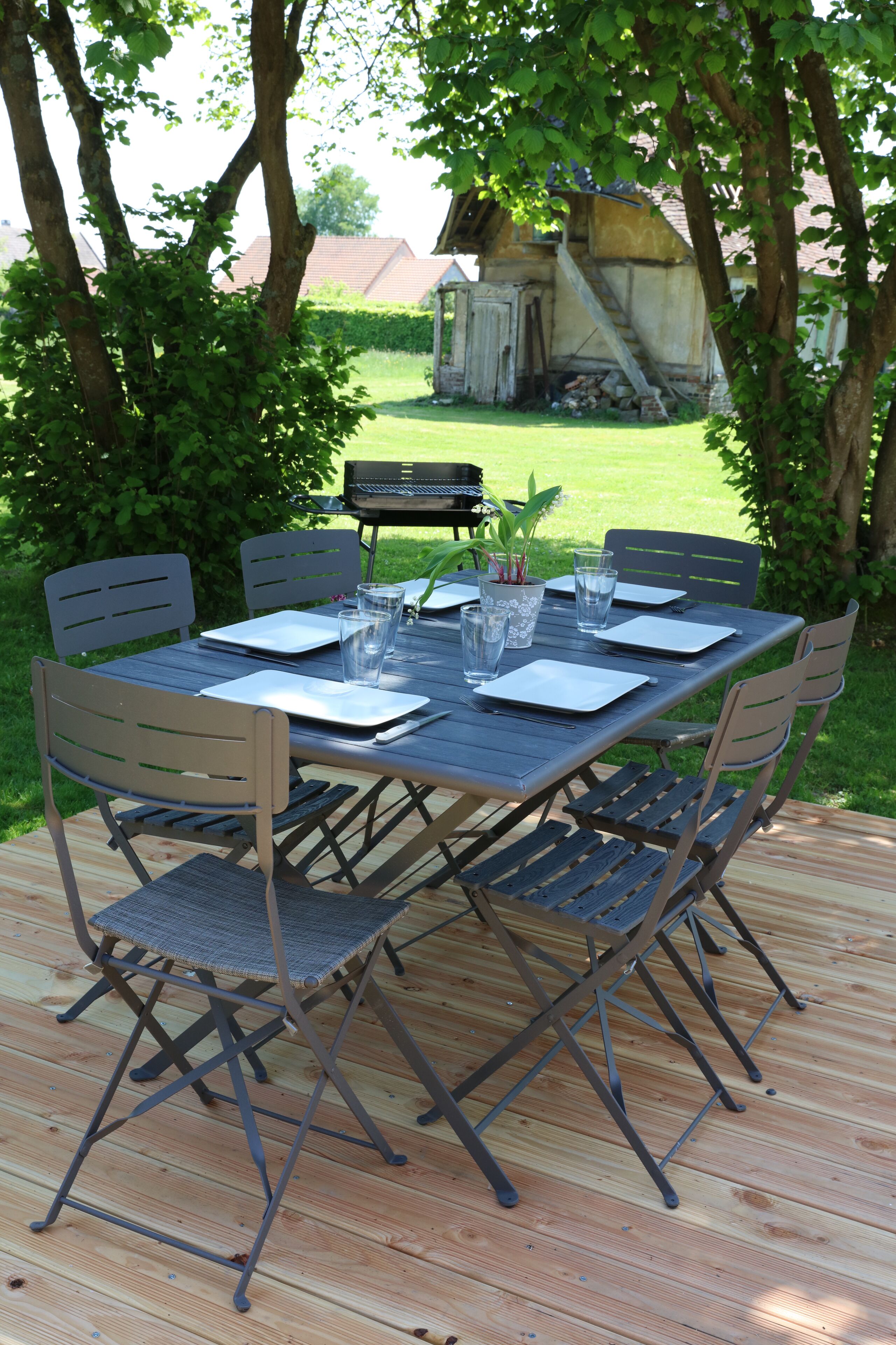 A wooden deck with a table set for four, surrounded by chairs.