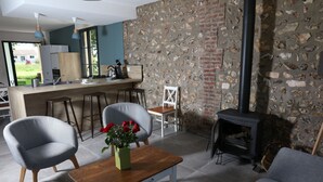 Una sala de estar moderna con una pared de piedra, una chimenea y una cocina visible a través de una puerta abierta.