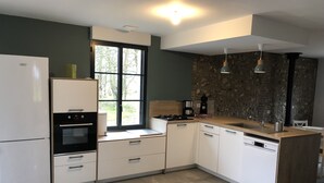 Una cocina moderna con armarios blancos, horno empotrado, lavavajillas, ventana con vistas a árboles y una pared de acento de piedra.