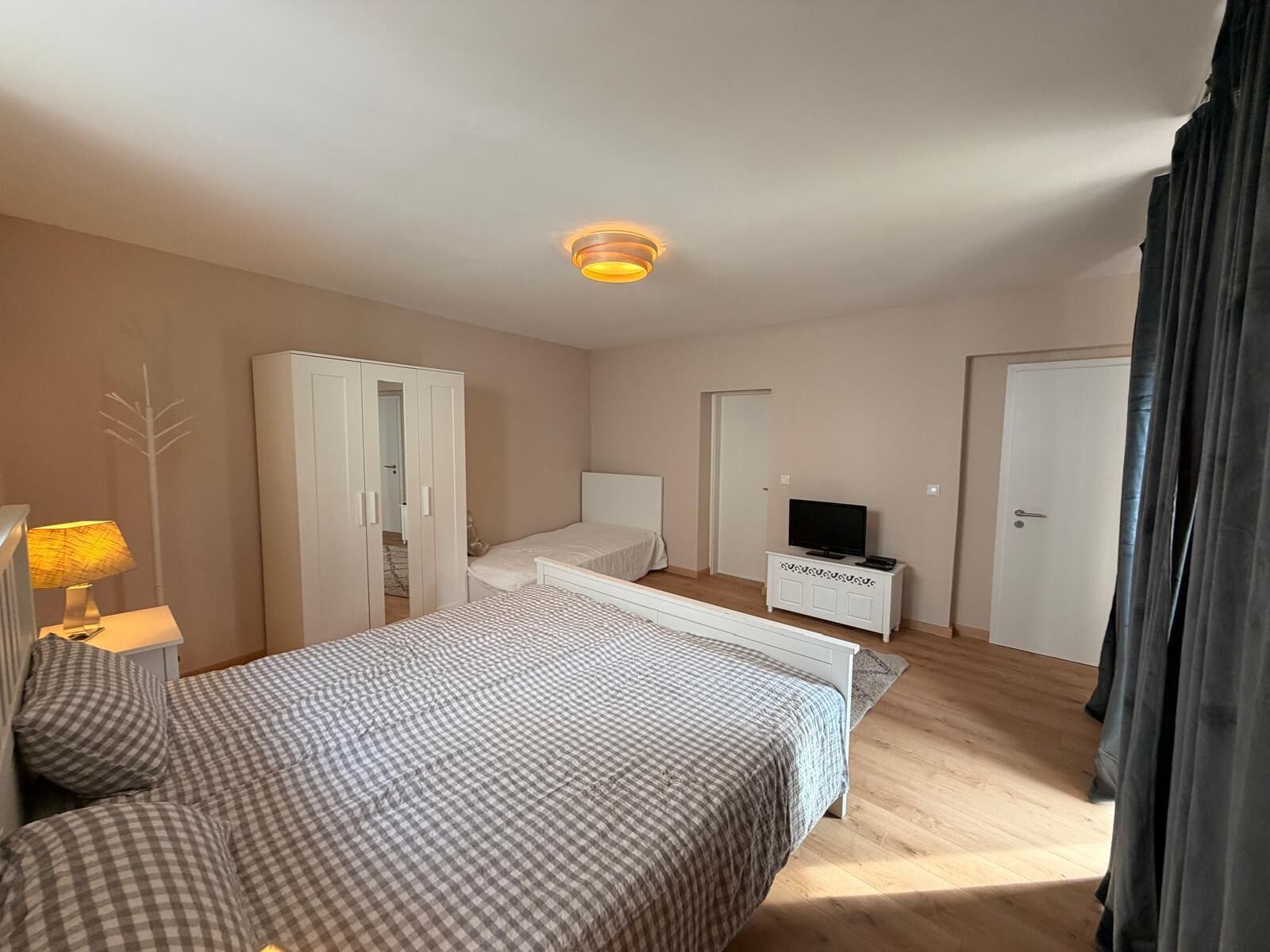 A bedroom with a bed, a wardrobe, a television on a side table, and a ceiling light.