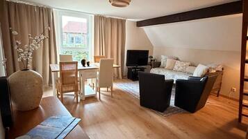 A room with a dining area, a sofa, and a TV.