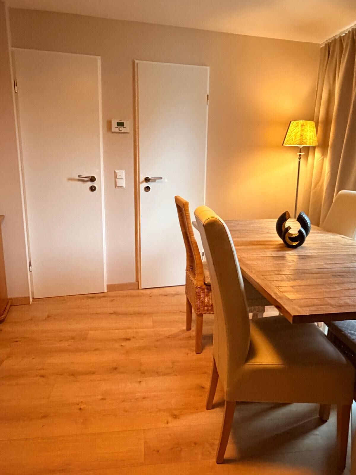 A dining area with a wooden table, four chairs, a lamp, and two doors.