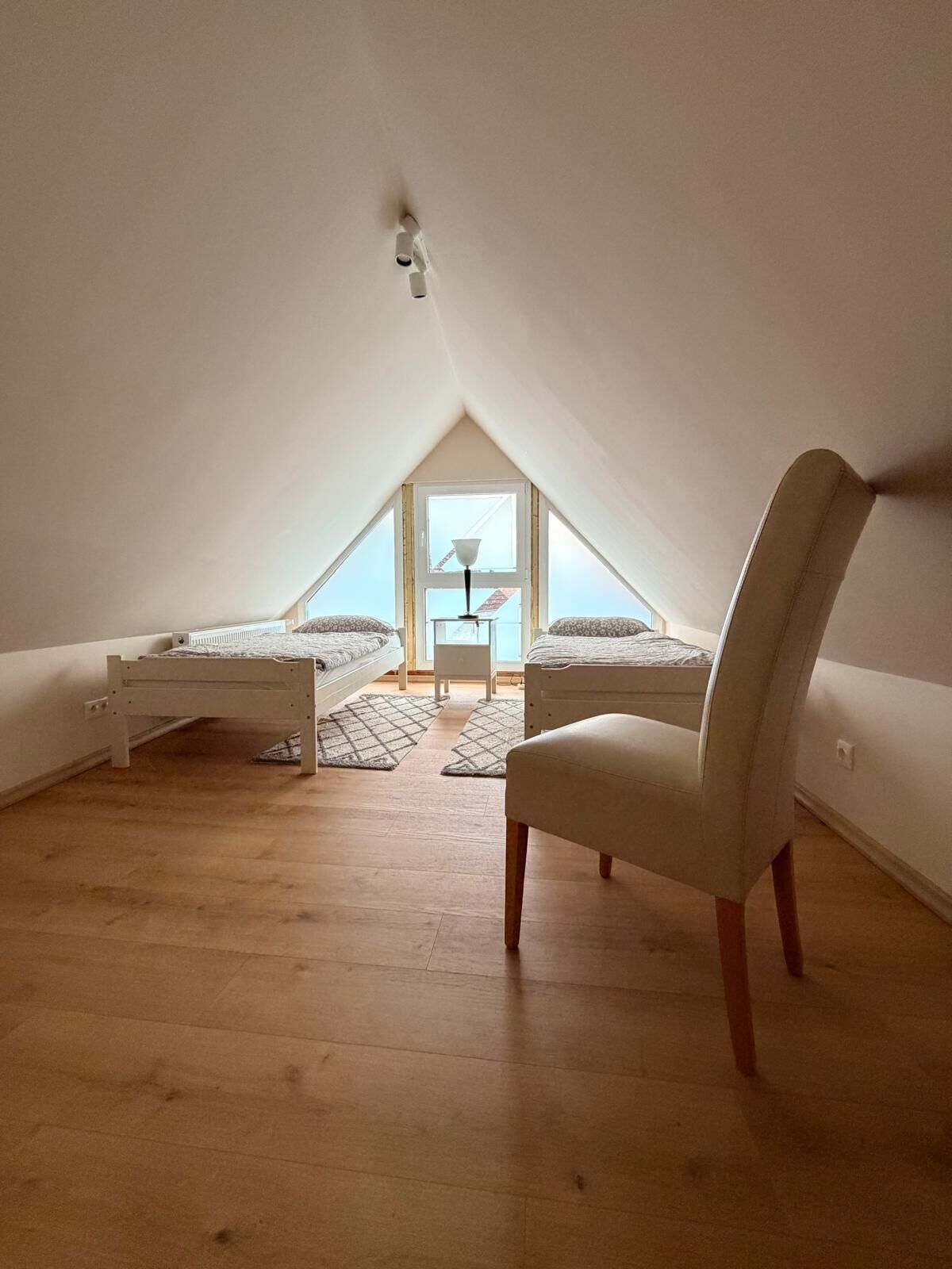 Pequeño dormitorio abuhardinado triangular con dos camas, una silla y una lámpara.