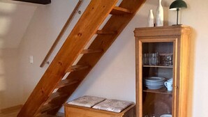A loft bedroom with a wooden staircase, a cabinet with glass doors, and a bench.