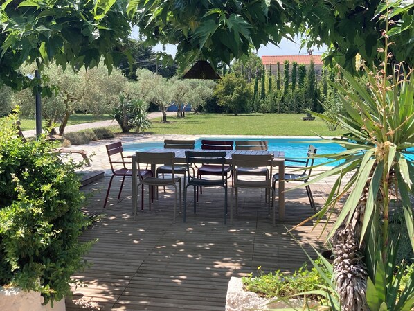 Et poolområde med træterrasse, et bord med stole og udsigt til en swimmingpool.