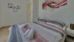 Una cama bien hecha con ropa de cama a rayas, una mesita de noche con un florero y una obra de arte abstracto colgada en la pared.